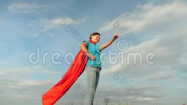 女孩梦想成为超级英雄。 年轻女孩站在红色斗篷里表达着梦想。 美丽的女孩超级英雄